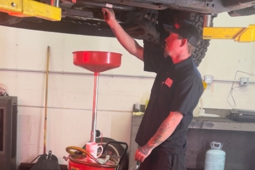 Oil change near me in Northglenn, CO with Accurate Automotive. Image of a mechanic performing an oil change maintenance on a lifted car by draining the oil first.