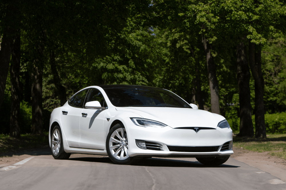tesla repair services, Auto Repair in Northglenn, CO at Accurate Automotive. White Tesla parked on a tree-lined road under bright sunlight.