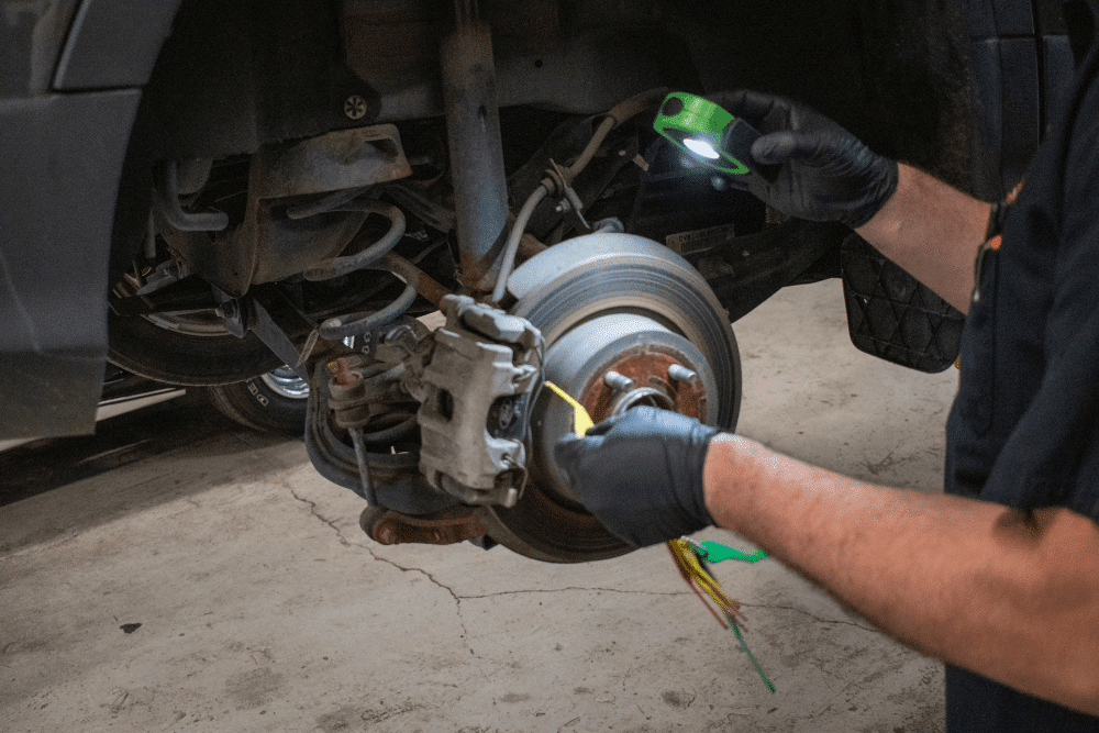 brake warning signs, Auto Repair in Northglenn, CO at Accurate Automotive. Mechanic inspecting a vehicle’s brake system with a flashlight and measuring tool.