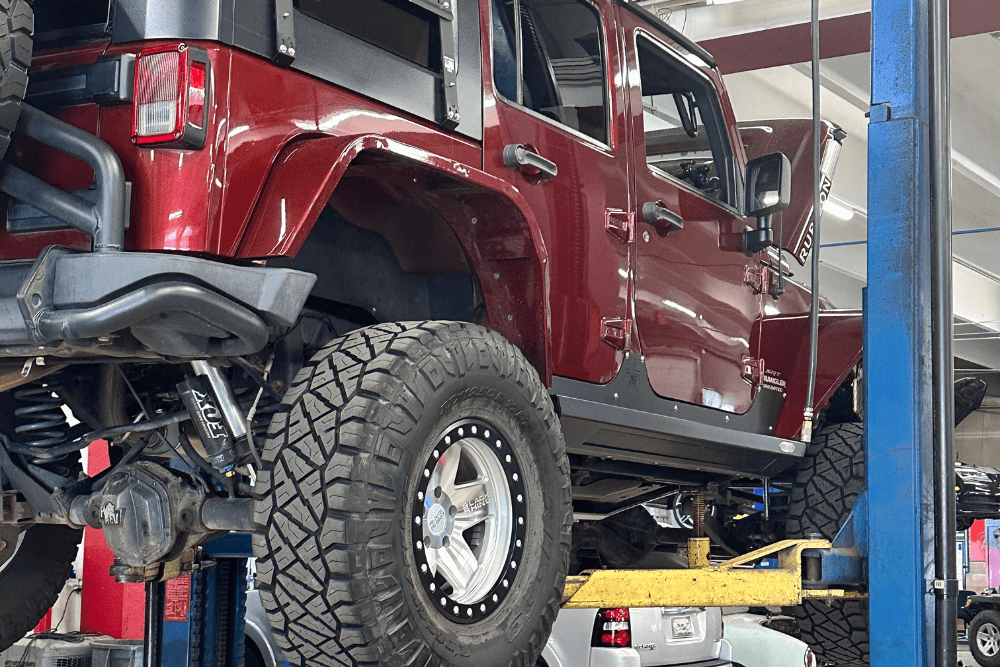 summer car prep, auto Repair in Northglenn, CO at Accurate Automotive. Jeep Wrangler lifted on a hydraulic car lift for suspension and driveline service at an Accurate Automotive repair shop.