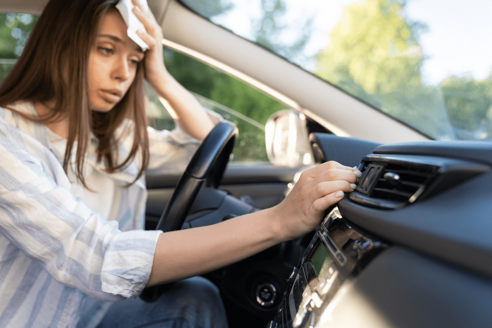 Car A/C repair in Northglenn, CO by Accurate Automotive. Image of a frustrated driver wiping sweat while adjusting car vents due to failing air conditioning.